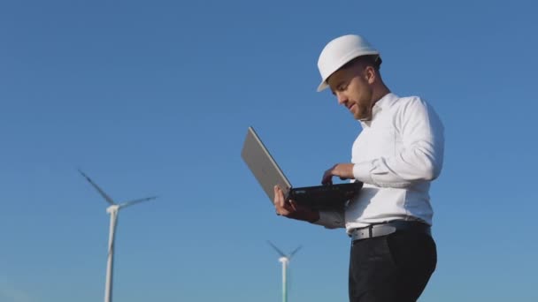 Inżynier w białym hełmie i klasycznej koszuli sprawdza pojemność elektrowni i robi notatki w laptopie. — Wideo stockowe