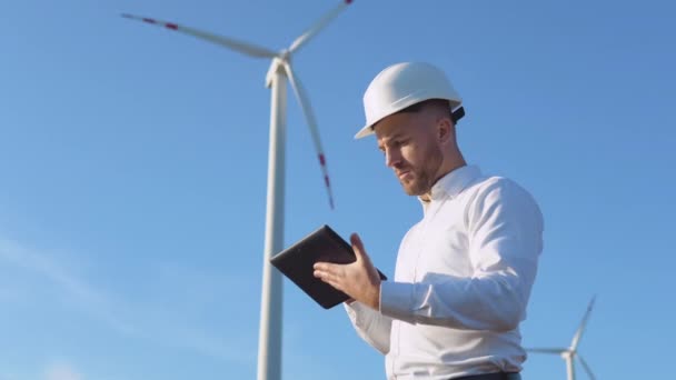 Ein männlicher Ingenieur mit weißem Helm und klassischem Hemd inspiziert die Leistung der Kraftwerke und macht sich Notizen auf einem Tablet. — Stockvideo