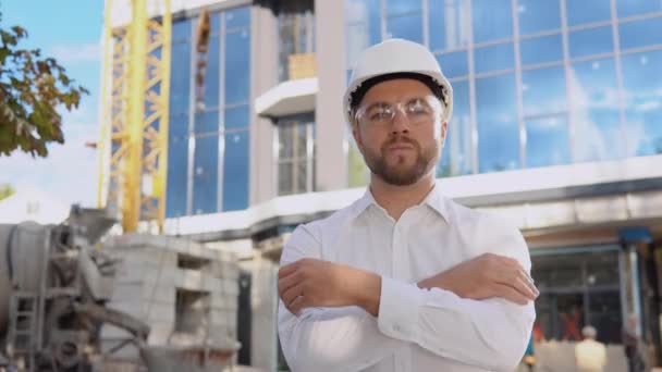 An engineer in a white shirt and helmet stands against the backdrop of a modern glass building. Modern construction — Stock Video