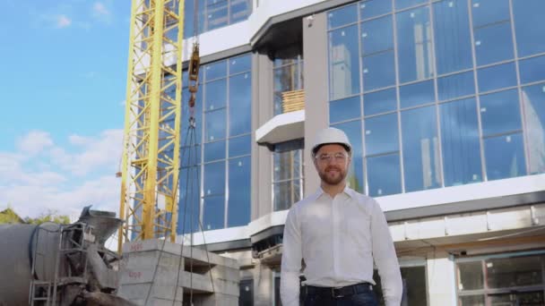 Egy mérnök fehér ingben és sisakban egy modern üvegépület hátterében áll. Modern építőipar — Stock videók