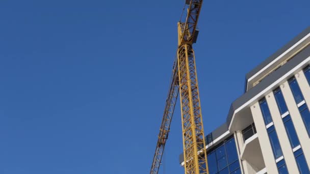 Grúa trabajando en obra bajo el cielo azul. Construcción de un moderno edificio de cristal — Vídeo de stock