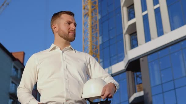 Architecte ingénieur en chemise blanche sur le fond d'un bâtiment en verre moderne et tenant un casque — Video