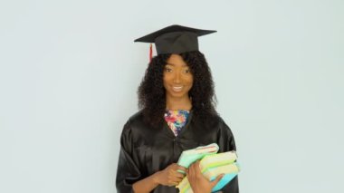 Siyah cüppeli ve şapkalı genç bir Afro-Amerikan kadın ders kitaplarını düz tutuyordu. Kameraya bakıyor. Yarım boy portresi