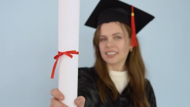 Ung kvinna student i svart klänning och en mästare hatt håller i sina händer i en upprätt position ett diplom av högre utbildning. En universitetsexamen dansar med ett diplom i händerna och nyser — Stockvideo