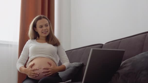 Pregnant fair-skinned woman communicates with loved ones via video on laptop — Stock Video