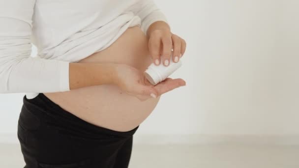 Schwangere hellhäutige Frau steht vor weißem Hintergrund und schüttet Tabletten auf die Handfläche — Stockvideo