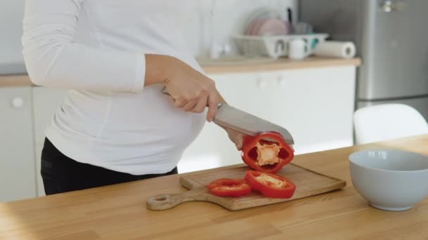 Gravid kvinna i köket skär röd paprika. Friska balanserad kost under graviditeten — Stockvideo