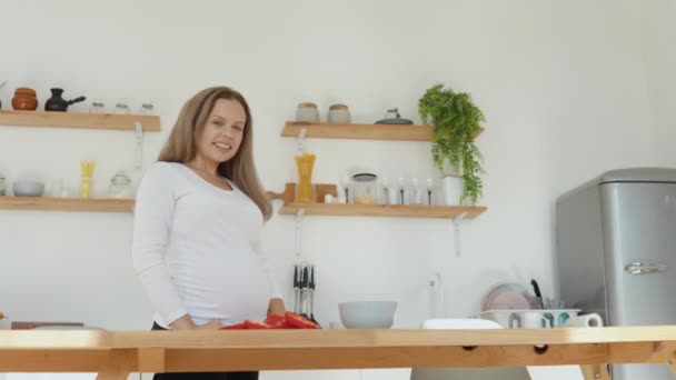 La mujer embarazada de piel clara en la cocina corta el pimiento rojo. Dieta sana y equilibrada durante el embarazo — Vídeos de Stock