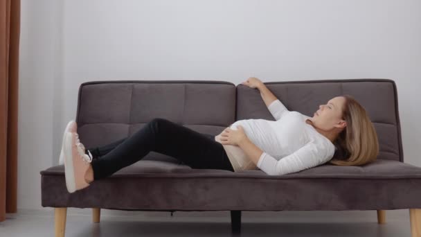 Έγκυος, ανοιχτόχρωμη γυναίκα με επίδεσμο προσπαθεί να σηκωθεί από τον καναπέ. — Αρχείο Βίντεο