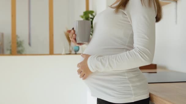 Terhes nő simogatja a hasát és teát iszik a konyhában. — Stock videók