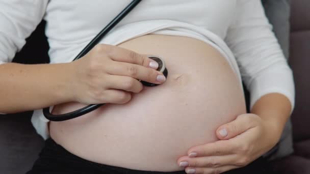 Une femme enceinte à la peau claire écoute les mouvements et les battements de cœur du fœtus avec un stéthoscope. — Video