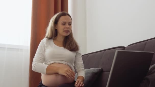 Schwangere hellhäutige Frau zeigt dem Gesprächspartner ein Foto von der Ultraschalluntersuchung des Fötus mittels Videoübertragung auf einem Laptop — Stockvideo