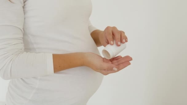 Schwangere steht auf weißem Hintergrund und schüttet Tabletten auf die Handfläche — Stockvideo