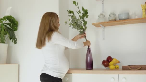 Беременная светлокожая женщина украшает дом эвкалиптовыми ветвями в вазе — стоковое видео