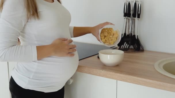 Беременная светлокожая женщина на кухне готовит быстрый питательный завтрак из хлопьев. Здоровое питание во время беременности — стоковое видео