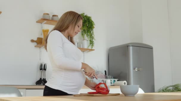 Беременная светлокожая женщина на кухне режет красный перец. Здоровое сбалансированное питание во время беременности — стоковое видео