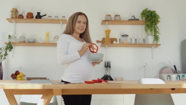 A mulher grávida de pele clara na cozinha corta pimenta vermelha. Dieta equilibrada saudável durante a gravidez — Vídeo de Stock
