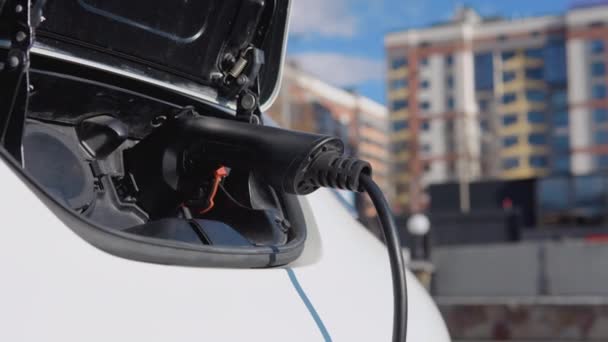 Mobil listrik mengisi baterai dengan listrik melalui kabel listrik di tempat parkir di daerah perumahan — Stok Video