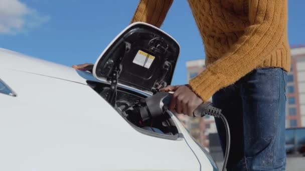 Африканський американський чоловічий водій з'єднує електричний автомобіль з системою живлення для заряджання автомобільної батареї. — стокове відео