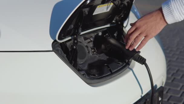 Açık tenli bir erkek sürücü elektrikli arabayı güç sisteminden ayırır. Yakın çekim görünümü — Stok video