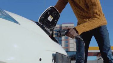 Afrikalı Amerikalı erkek sürücü elektrikli arabayı araba aküsünü şarj etmek için güç sistemine bağlıyor