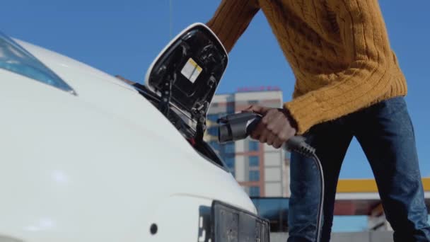 Αφρικανική αμερικανική αρσενικό οδηγό συνδέει ηλεκτρικό αυτοκίνητο με το σύστημα ηλεκτρικής ενέργειας για τη φόρτιση της μπαταρίας του αυτοκινήτου — Αρχείο Βίντεο