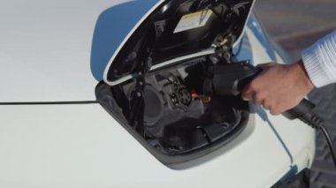 Açık tenli bir erkek sürücü elektrikli arabayı şarj etmek için güç sistemine bağlar.