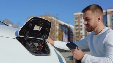 Bir erkek sürücü elektrikli arabayı şarj etmek için güç sistemine bağlar.