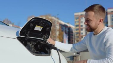 Açık tenli bir erkek sürücü elektrikli arabayı güç sisteminden ayırıyor.