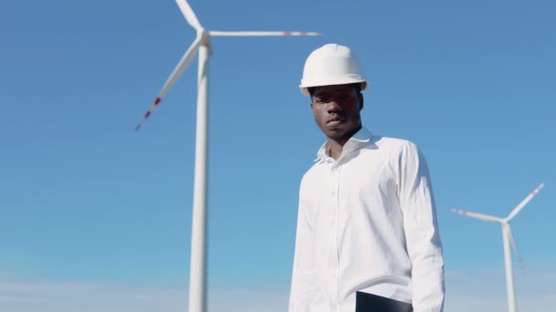 Ingénieur électricien afro-américain debout sur le fond d'un moulin à vent dans une centrale à air. Turbines éoliennes produisant des énergies renouvelables propres — Video