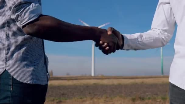 Két afro-amerikai férfi villamosmérnök áll egy szélmalom hátterében egy légi erőműben, és kezet ráznak. Közelkép a kezekről — Stock videók