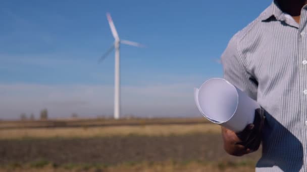 Ingegnere elettricista afroamericano in piedi sullo sfondo di un mulino a vento in una centrale elettrica ad aria con un disegno in mano. Vista ravvicinata di mano e scorrimento — Video Stock