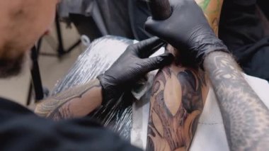 Dövme makinesiyle dövme yapma işlemi. Dövme salonundaki bir erkeğin elinde kadın yüzü..