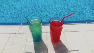 Blue and red cocktails with ice stand on side pool, against background of pool, blue water. Summer pool party, vacation