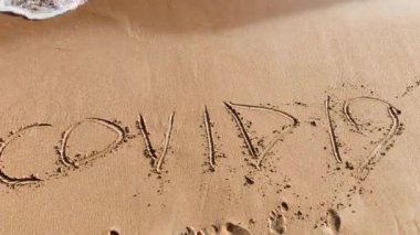 The inscription covid 19 in the sand is washed away by the waves