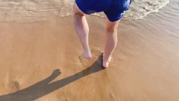 Забавна людина в блакитних шортах танцює на пляжі. Босоногі чоловічі ноги танцюють на піску біля моря — стокове відео
