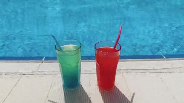 Summer pool party, vacation. Blue and red cocktails with ice stand on side pool, against background of pool, blue water — Video Stock