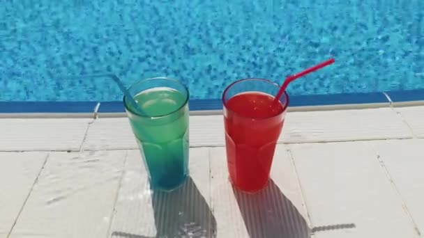 Blue and red cocktails with ice stand on side pool, against background of pool, blue water. Summer pool party, vacation — Stock Video