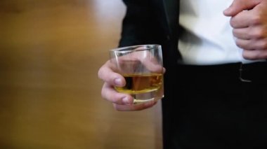 Attractive business man with a glass of whiskey in a brown room. Businessman holding whiskey