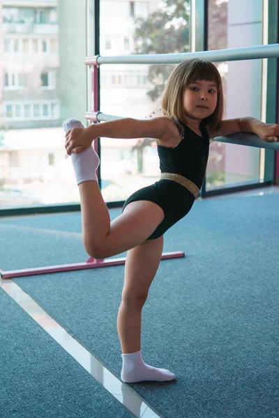 Gadis pesenam cantik dengan leotard hitam melakukan latihan peregangan. Potret vertikal Stok Lukisan  