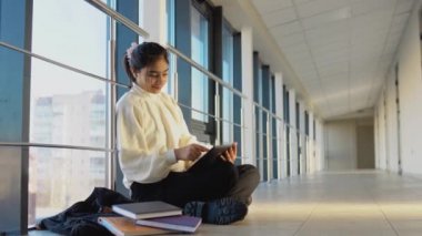 Indian girl student sitting on the floor with a tablet in the university or college. New modern fully functional education facility. Concept of online education