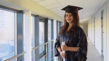 Pakistani female graduate in mantle stands with a diploma in her hands and smiles