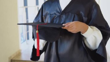 Indian female graduate in mantle stands with a hat in her hands. Closeup