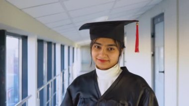 Indian female graduate in mantle stands with a diploma in her hands and smiles