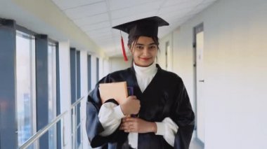 Indian female graduate in mantle stands with a books in her hands and smiles. A graduate of a medical university with a books