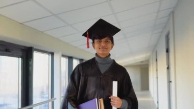 Pakistani graduate in mantle stands with a diploma and books in her hands and smiles. An important event. Young specialist