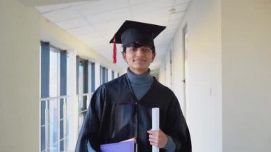 Indian male graduate in mantle stands with a diploma and books in her hands and smiles. An important event. Young specialist