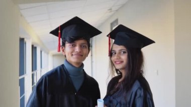 Two Indian graduates stand in the corridor of the university and look at the camera. Education concept