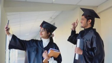 Two Indian graduates stand in a university hallway and take a selfie. Education concept