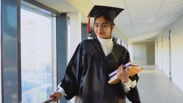 Indian female graduate in mantle stands with a books in her hands and smiles. A graduate of a medical university with a diploma — Wideo stockowe